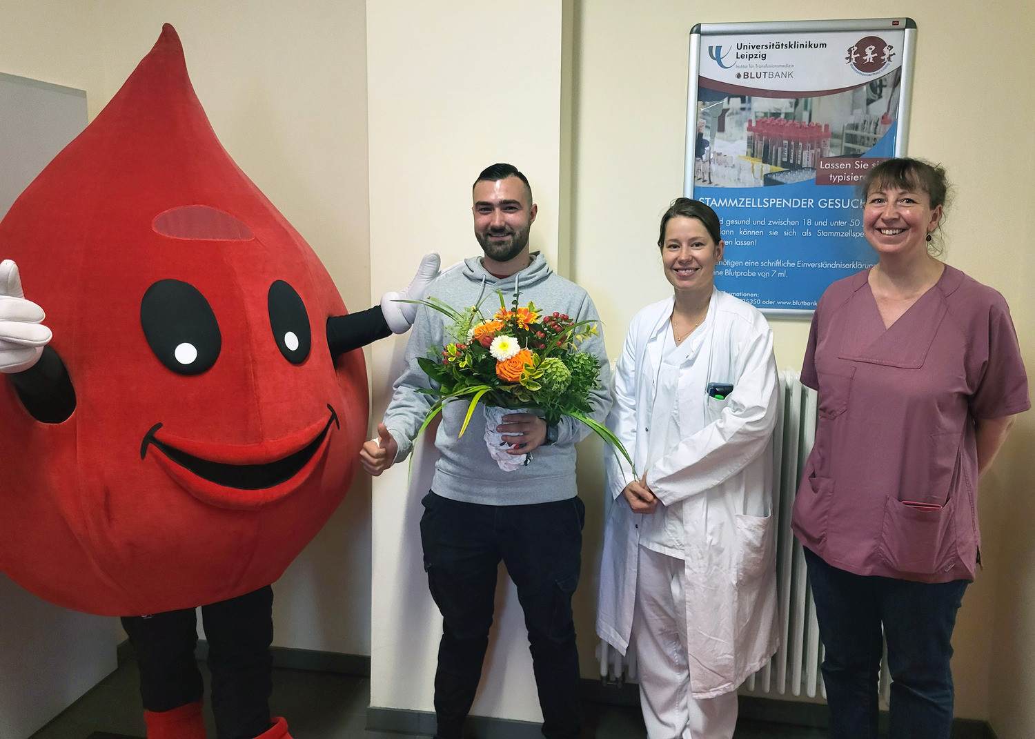 Maskottchen Blutbert, Dr. Lisa-Marie Dilz (2. v. r.) und Dr. Rebecca Großmann vom ITM bedankten sich bei Stammzellspender Niclas Wittmann mit einem großen Blumenstrauß für dessen Engagement.